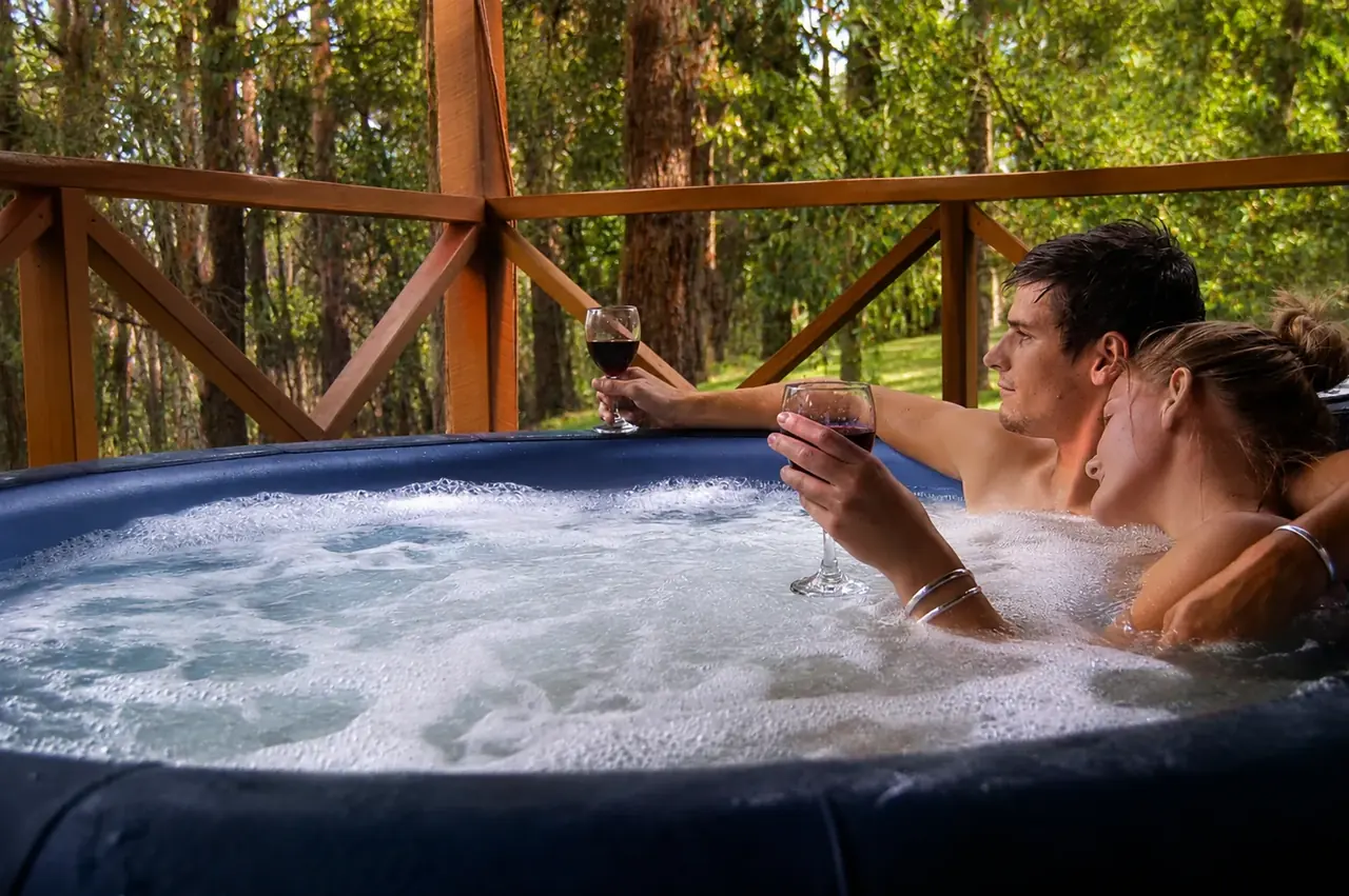 A couple relaxing with a glass of wine in the private heated spa on a chalet verandah
