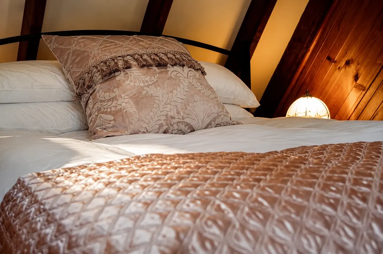 The mezzanine bed under the pitched roof, warm under lamplight